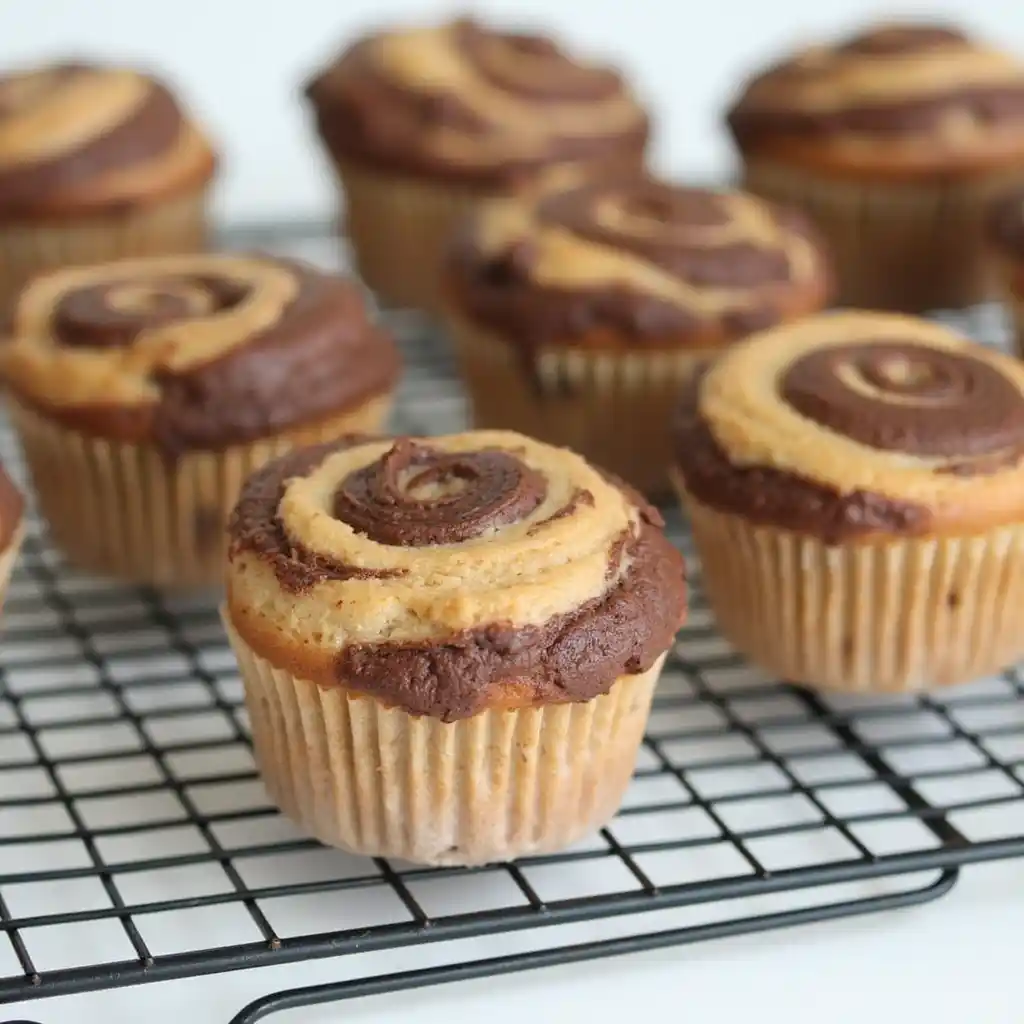 A stack of Banana Chocolate Swirl Muffins on a white plate, garnished with chocolate chips and banana slices